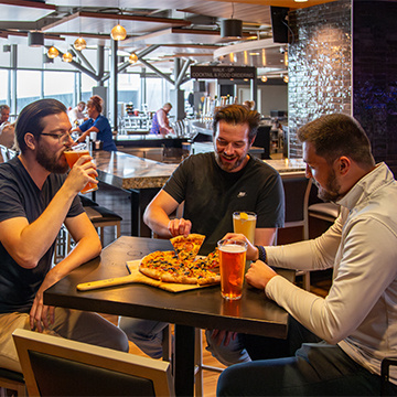 Three young guys eating pizza and drinking beer in an airport