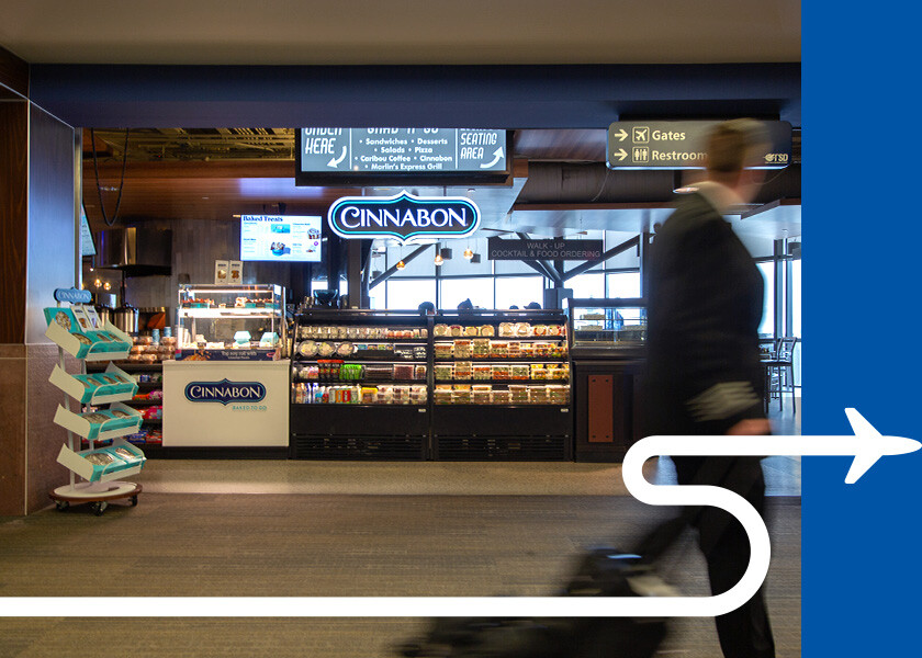 Cinnabon sign in an airport with pilot walking by